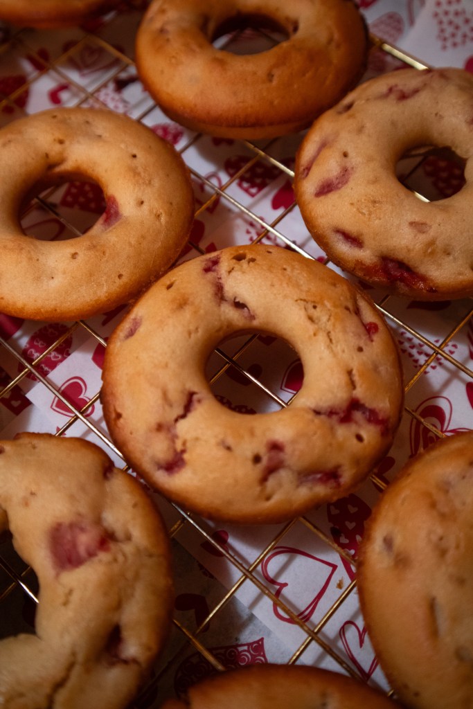 Freshly baked strawberry-flavored donuts on a cooling rack.