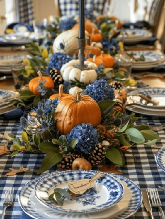A festive Thanksgiving tablescape featuring a blue and white checkered tablecloth, decorated with pumpkins, blue hydrangeas, pinecones, and an elegant candle centerpiece, creating a warm and inviting atmosphere.