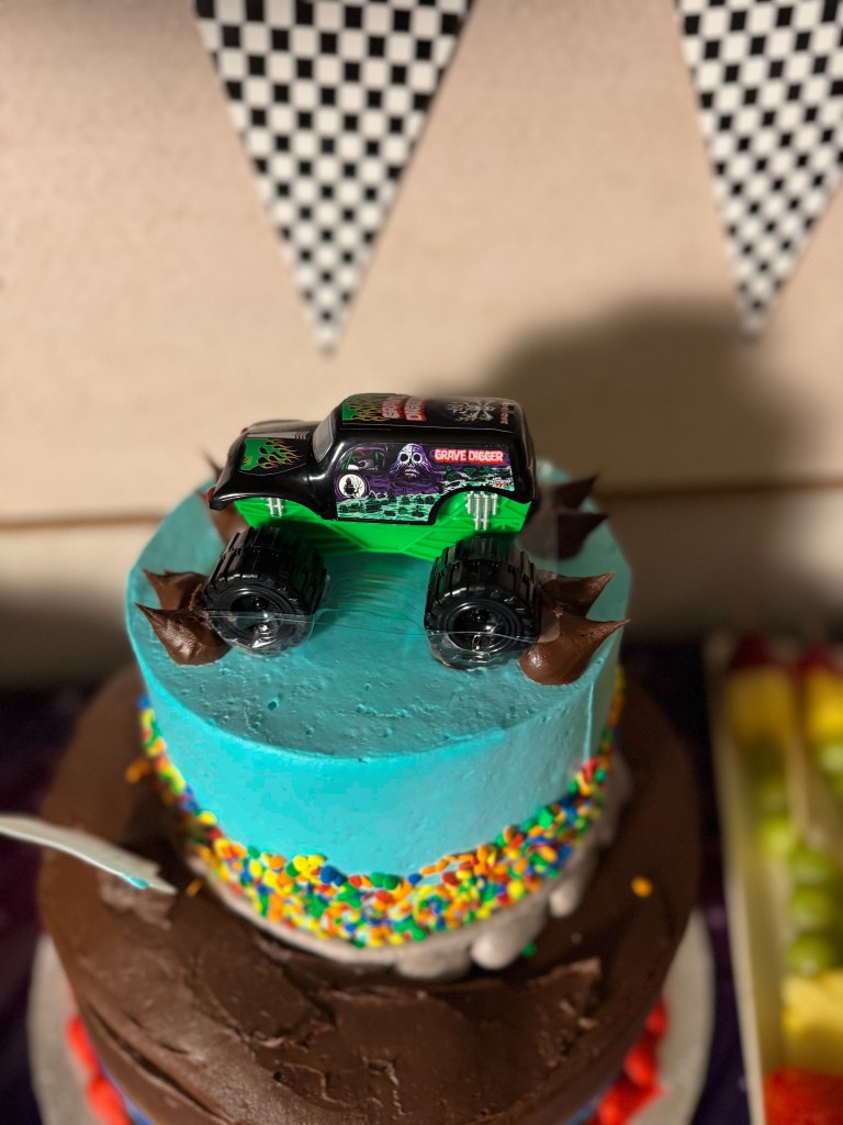 Monster Jam birthday cake with Grave Digger toy monster truck topper and colorful sprinkles on a racing themed party cake.