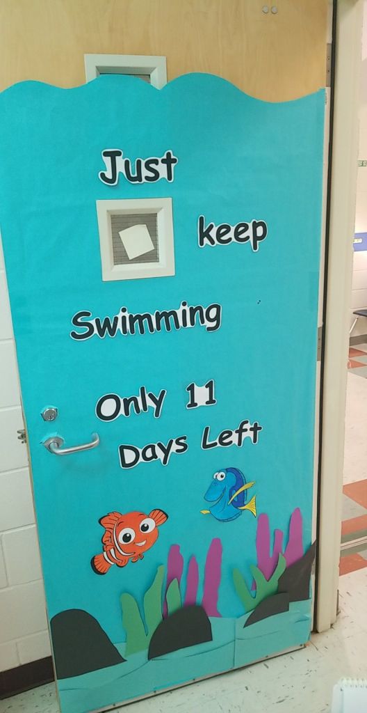 A decorative classroom door featuring an ocean theme with the phrase 'Just keep Swimming' and 'Only 11 Days Left' prominently displayed. Two cartoon fish are illustrated at the bottom among colorful seaweed.