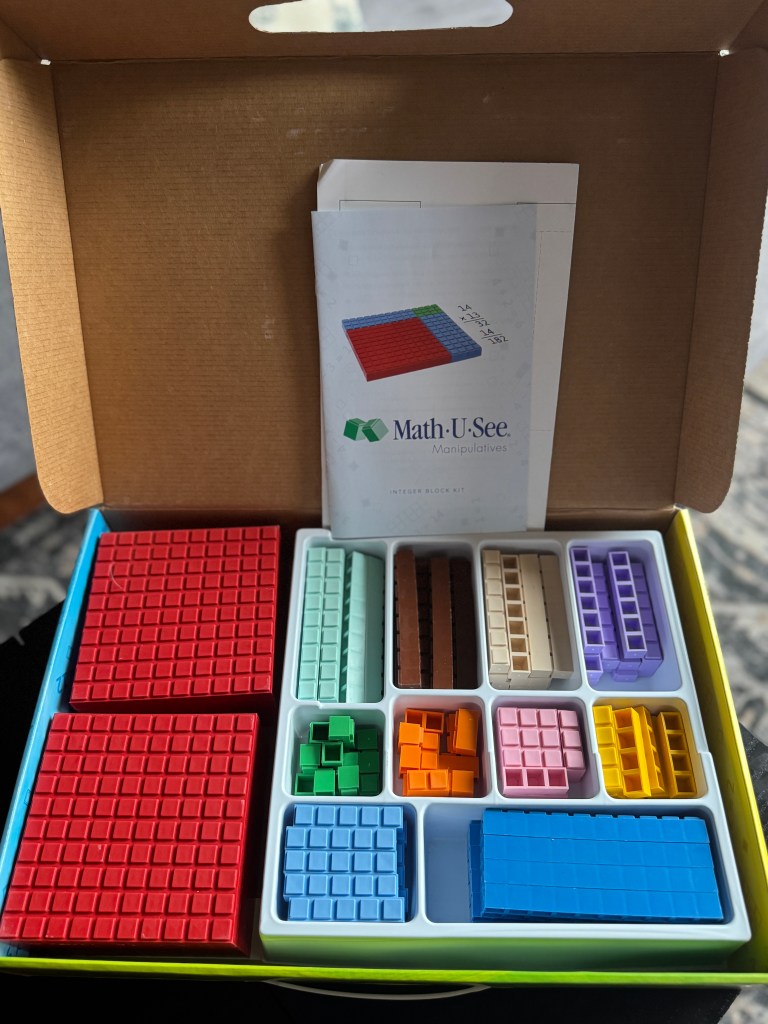 An open box displaying the Math-U-See Integer Block Kit, featuring colorful manipulatives organized in a neatly arranged tray alongside the instructional manual.