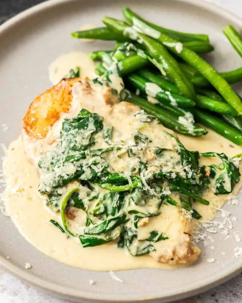 A serving of creamy garlic chicken breast on a plate, accompanied by fresh green beans.