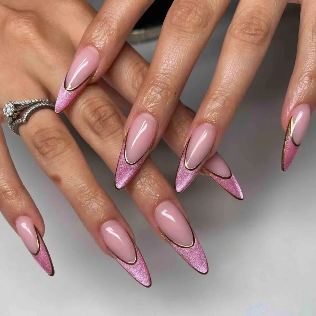 Close-up of manicured hands with long, almond-shaped nails featuring a gradient pink design with metallic gold accents.
