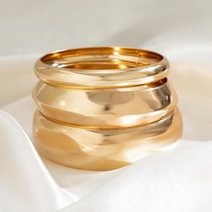 A set of three gold bangles stacked together on a soft, light-colored fabric.