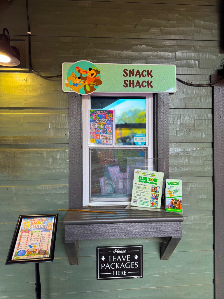 A colorful 'Snack Shack' window with a playful sign featuring characters, displaying menus and promotional materials, alongside a sign instructing to leave packages.
