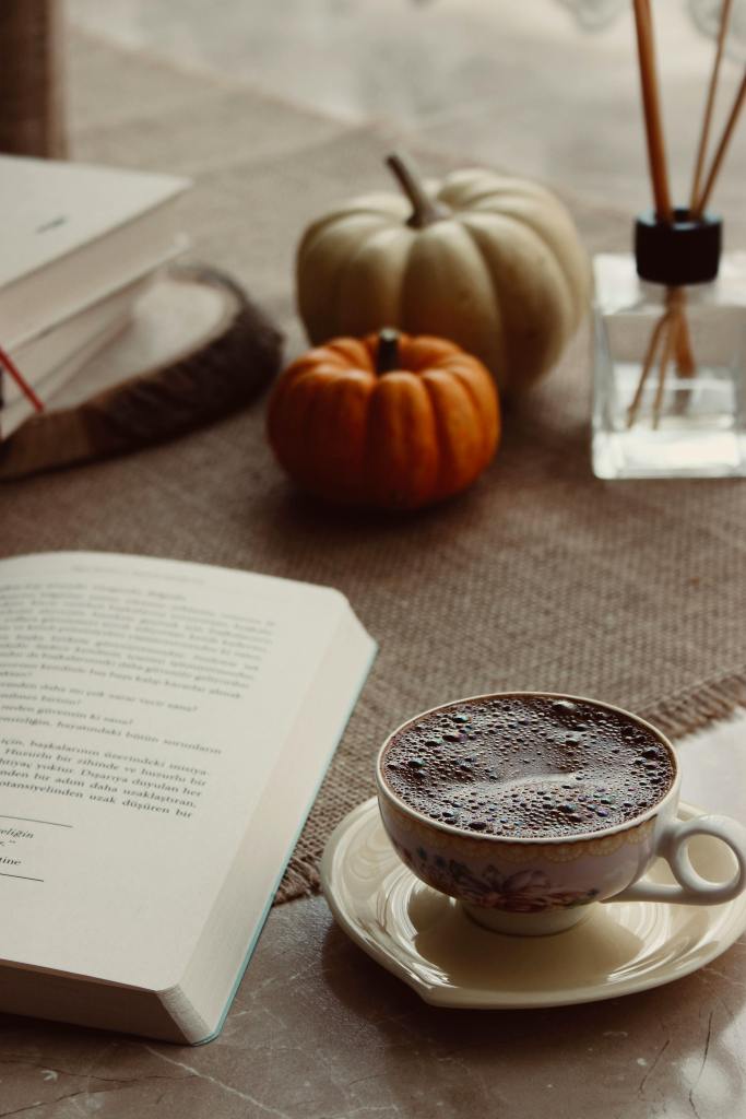 A cozy autumn scene featuring a book, a cup of coffee, and decorative pumpkins on a rustic table.