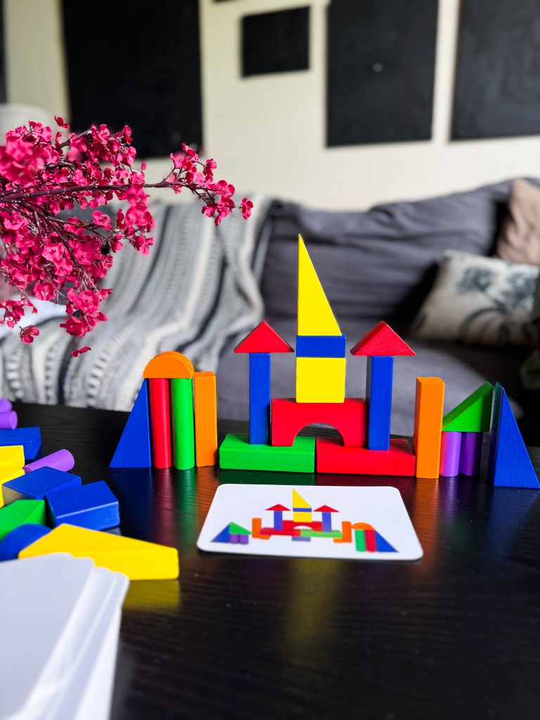 Colorful building blocks arranged to form a castle-like structure, with a pink flower branch in the foreground and a reference card showing the design beside it.