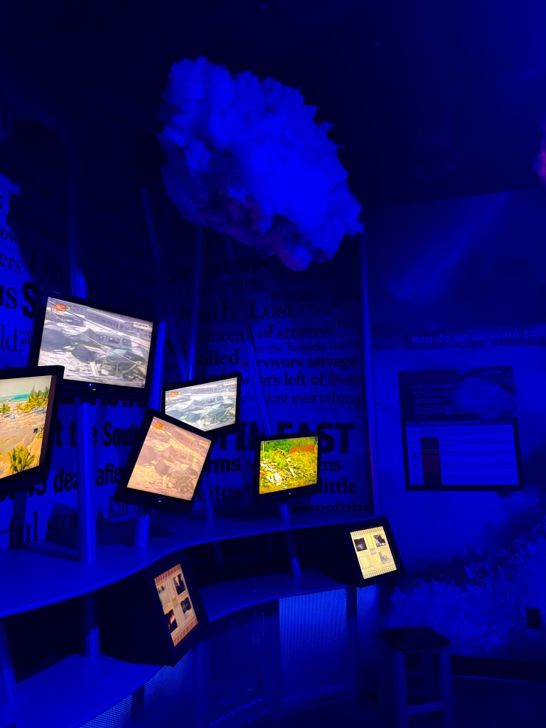Interactive display featuring multiple screens showcasing storm damage and meteorological information, illuminated by blue lighting.
