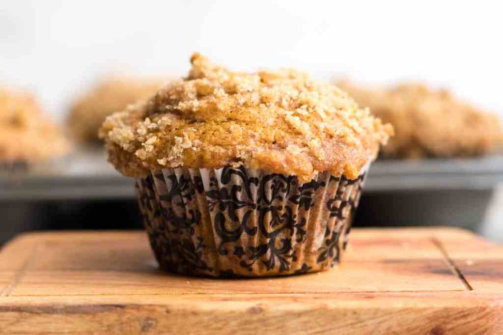 A freshly baked pumpkin muffin topped with a crumbly streusel, placed on a wooden surface.