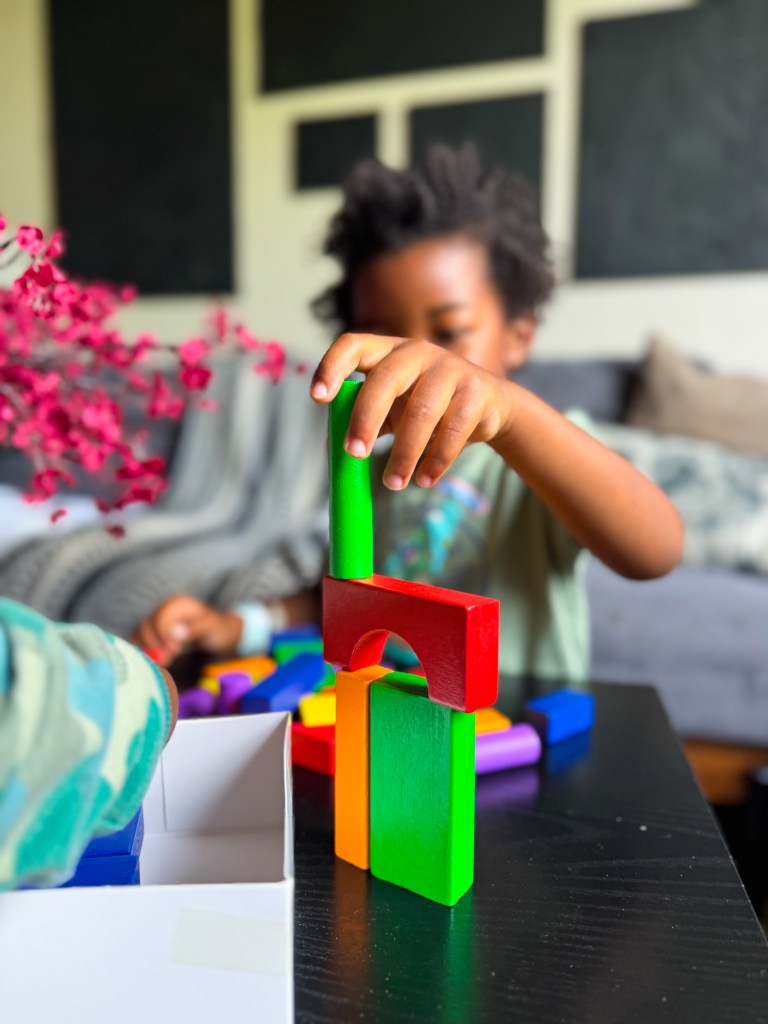 A child stacking colorful wooden blocks on a table, focused on building a structure, with various blocks scattered around.