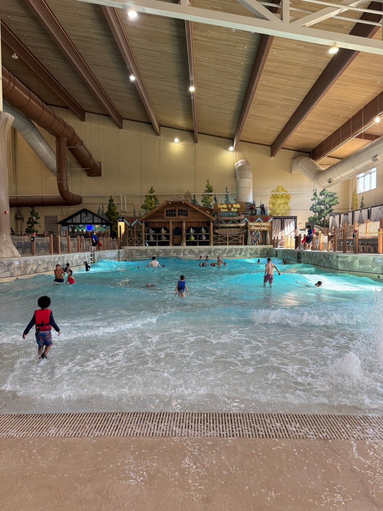 Indoor water park at Great Wolf Lodge featuring a wave pool, kids playing in the water, and themed decor in the background.