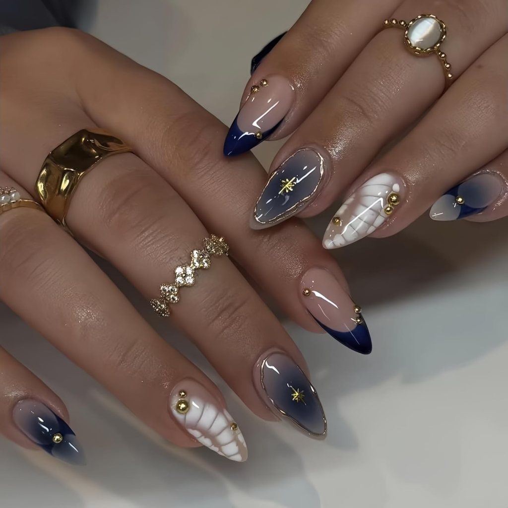 Navy blue and white sweater-inspired almond nails with gold studs and glossy ombre French tip accents.