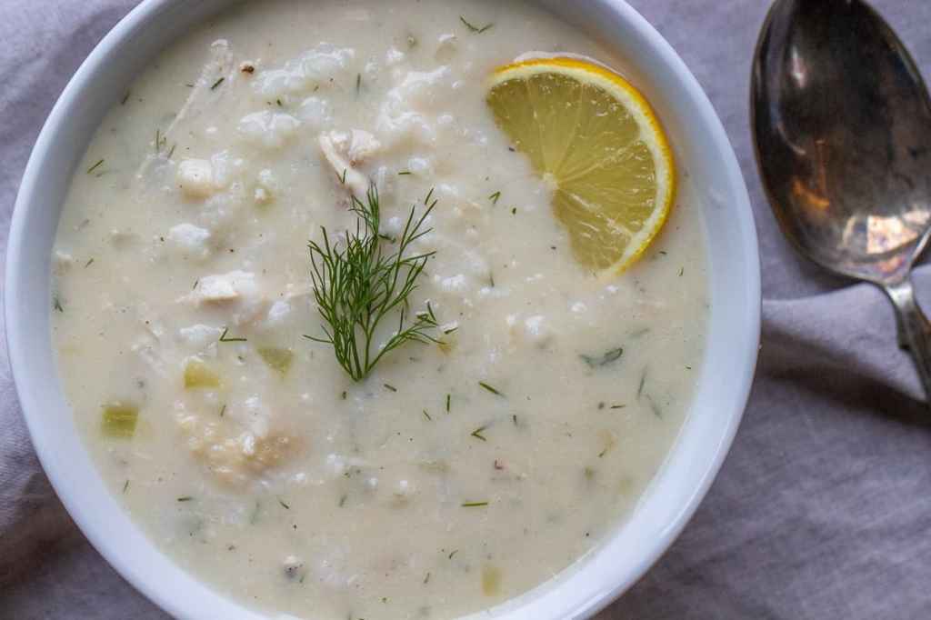 A bowl of creamy soup garnished with a slice of lemon and fresh dill, served on a light fabric surface.