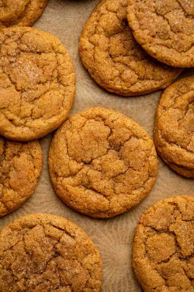 Close-up of freshly baked pumpkin cookies, golden brown and slightly cracked, arranged on parchment paper.