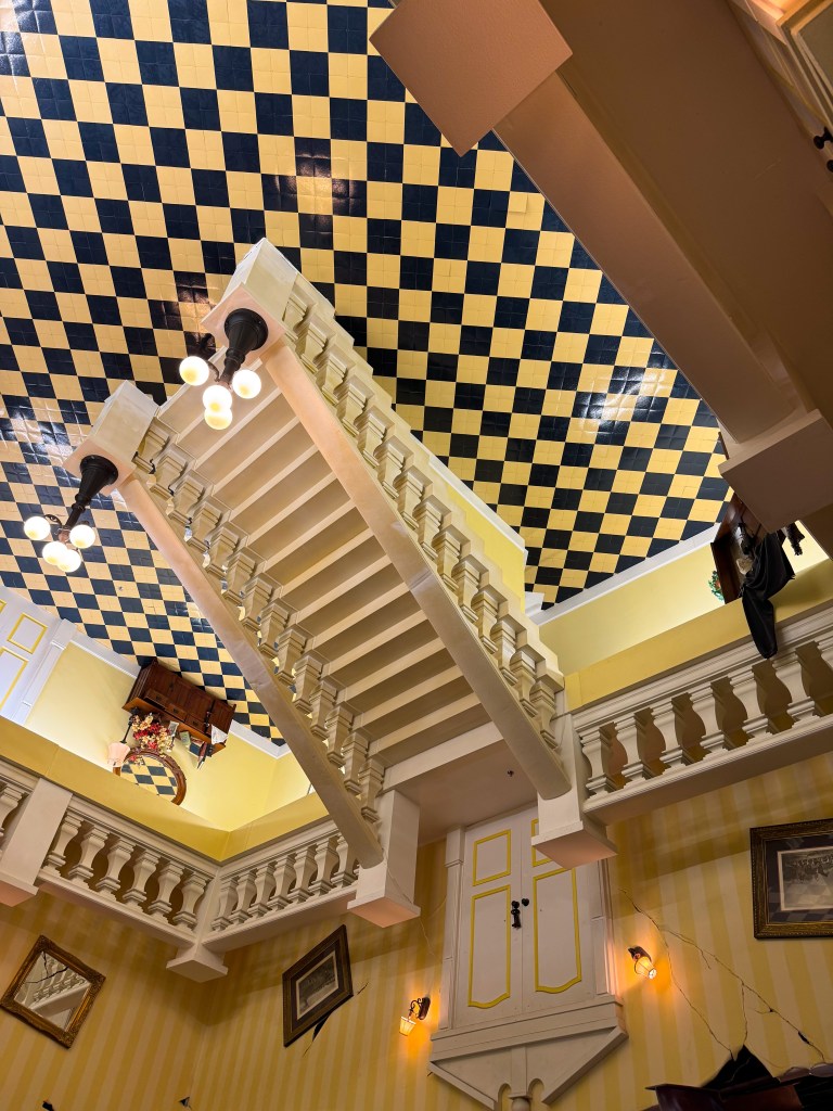 A view of a staircase leading upward, with a checkered yellow and black ceiling and decorative wall features.