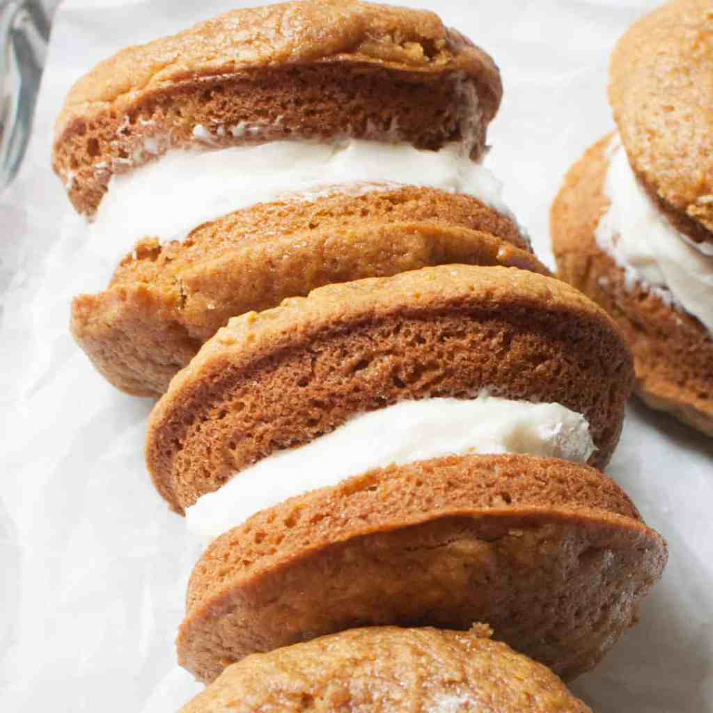 Close-up of pumpkin whoopie pies filled with creamy frosting, arranged neatly on a sheet of parchment paper.
