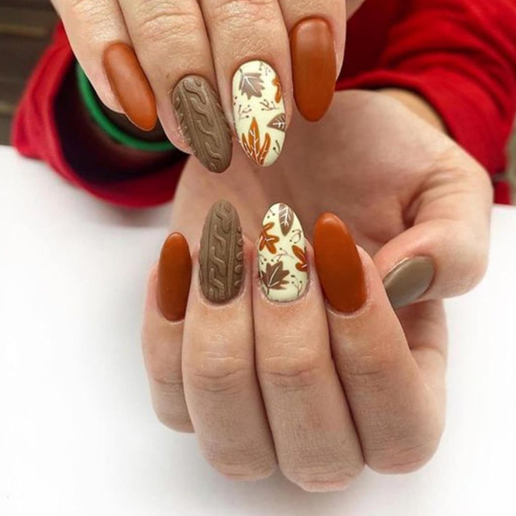 Close-up of hands showcasing Thanksgiving-themed nail art, featuring burnt orange, chocolate brown, and cream hues with intricate leaf designs and textured patterns.