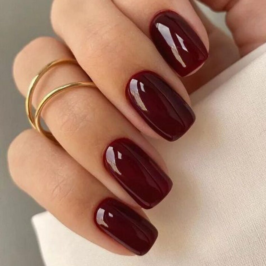 Close-up of a hand with stylish burgundy nail polish and two gold rings.