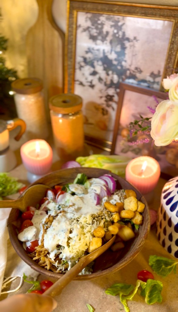 A beautifully arranged bowl of salad featuring shredded chicken, cheese, cherry tomatoes, sliced onions, and creamy dressing, surrounded by candles and decorative elements.