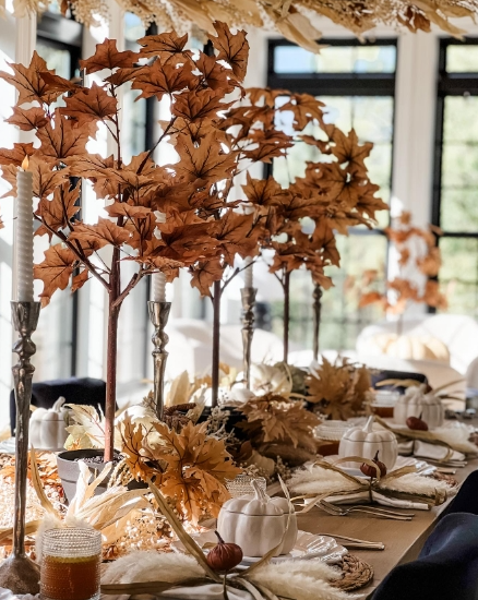 A beautifully styled fall tablescape featuring decorative branches with orange leaves, elegant candle holders, soft white pumpkins, and natural-colored accents, creating a warm and inviting atmosphere.