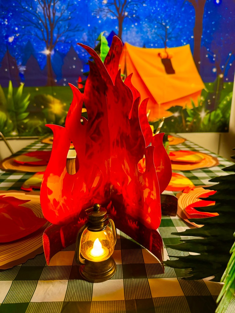 Cozy indoor campsite party table with lantern lights and campfire decorations.