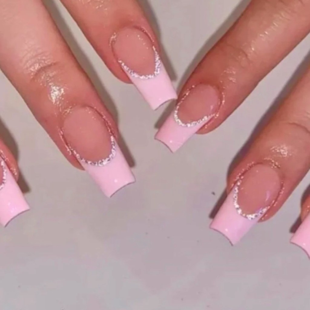 Close-up of hands displaying long, pink French tip nails with a glittery design.