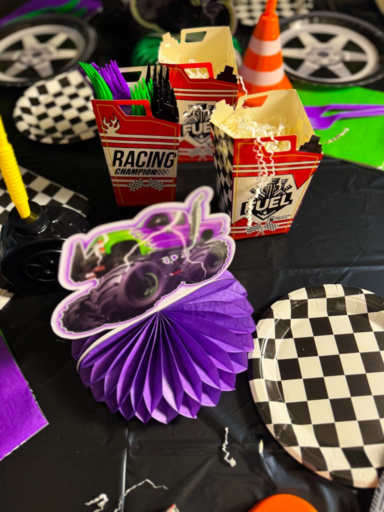 Monster Jam birthday party table decorations with checkered racing plates, monster truck centerpiece, and themed fuel snack boxes.