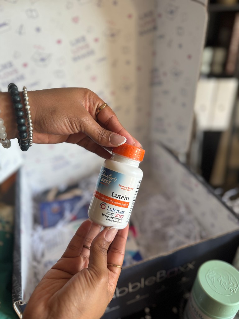A hand holding a bottle of Doctor's Best Lutein, a dietary supplement aimed at supporting eye health and cognitive function, with a colorful background and a partially visible box of BabbleBoxx.