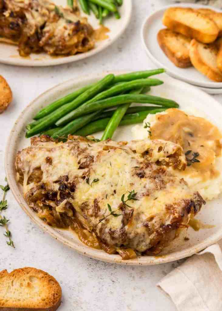 A plate featuring creamy garlic chicken topped with melted cheese, served with green beans and toasted bread slices.