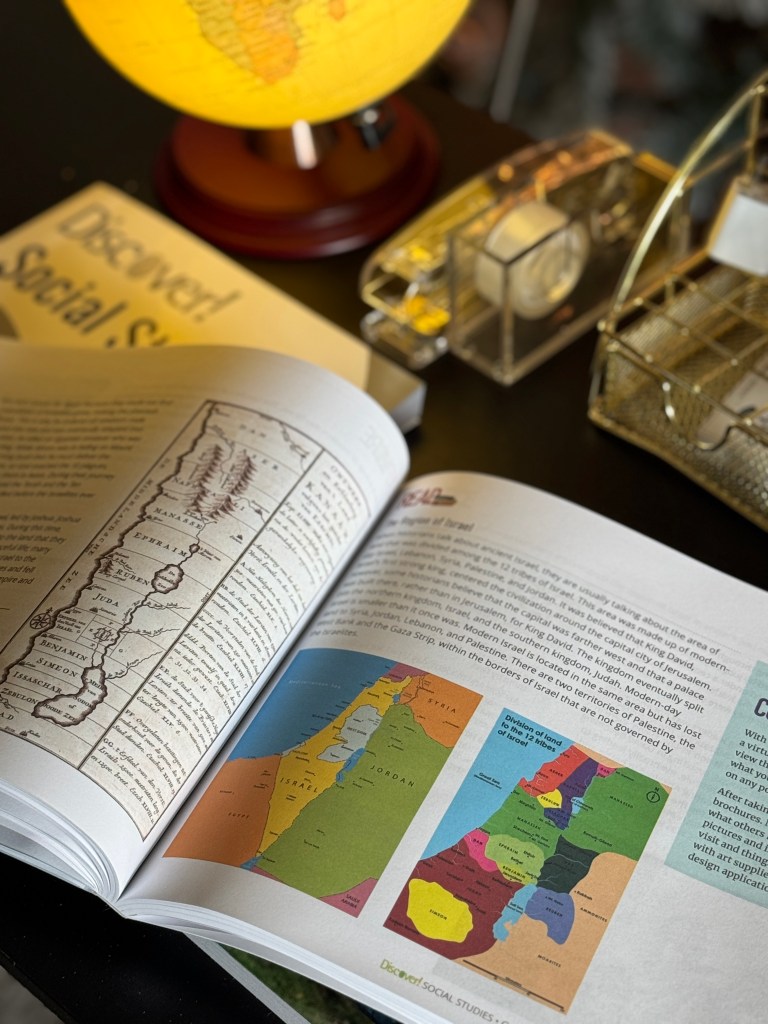 An open social studies textbook displaying maps of Israel, with a globe and other supplies on a table.