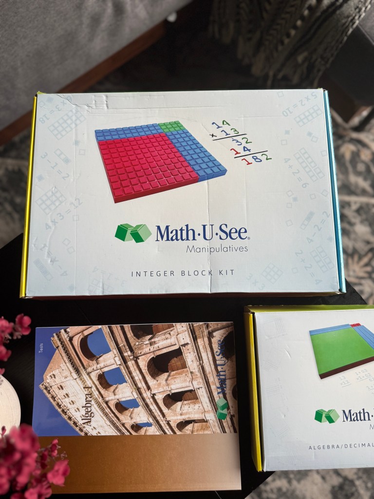Math-U-See Algebra 1 Integer Block Kit box with manipulatives, featuring red, green, and blue blocks, and math equations on the top, alongside the student workbook and other materials.