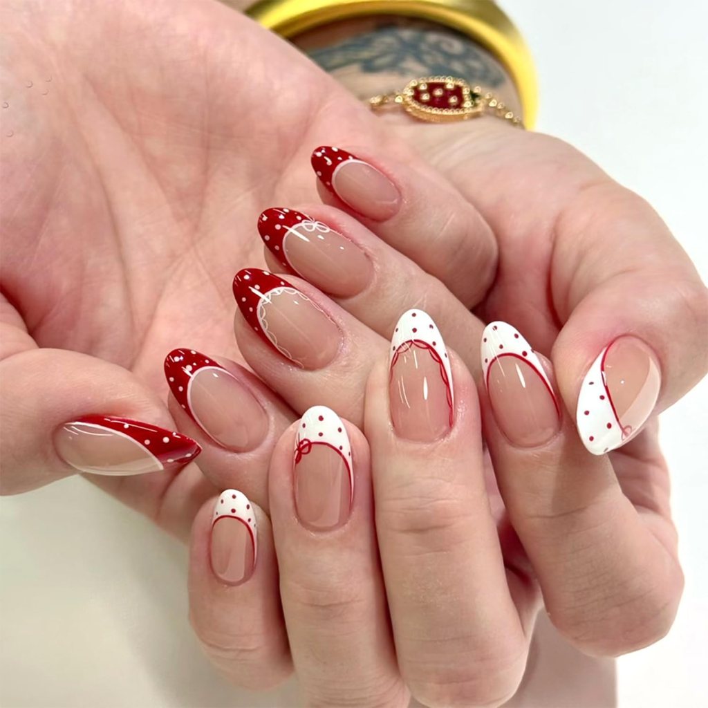 A close-up of hands featuring manicured nails with red and white nail art, including polka dots and decorative lines.