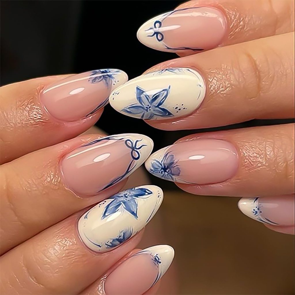 Close-up of hands showcasing elegant pointed nails with floral designs in blue and white.