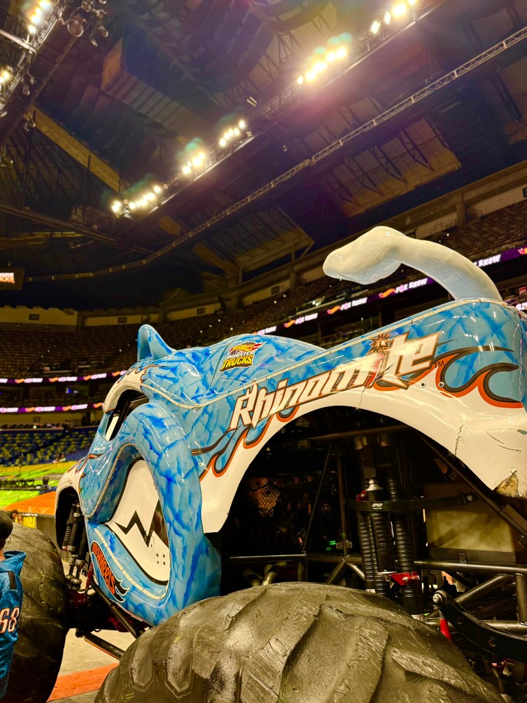 Side view of the blue Rhinomite monster truck with its horn, tail and oversized tires.