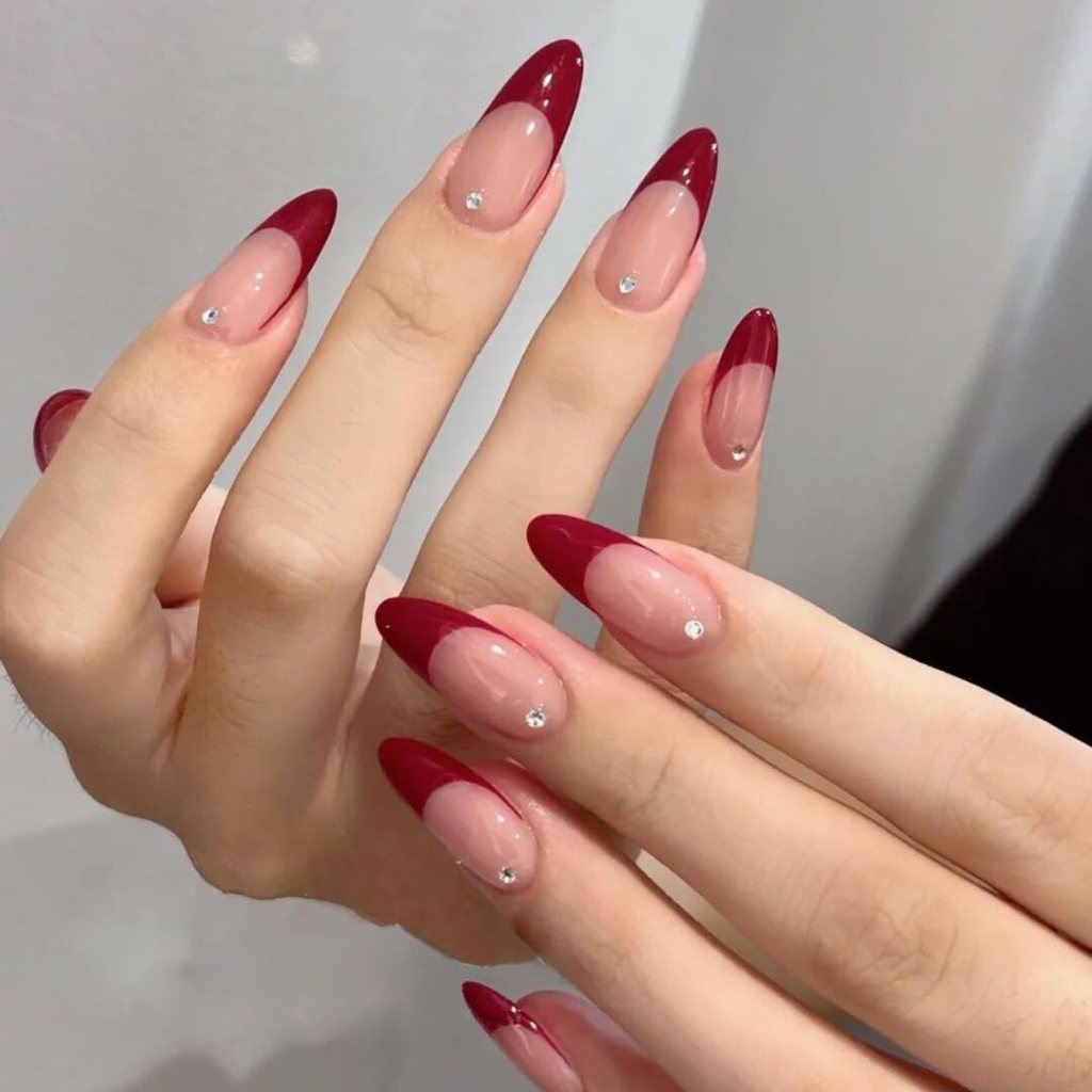 Close-up of hands with stylish manicure featuring red-tipped nails and rhinestone accents on a pastel base.