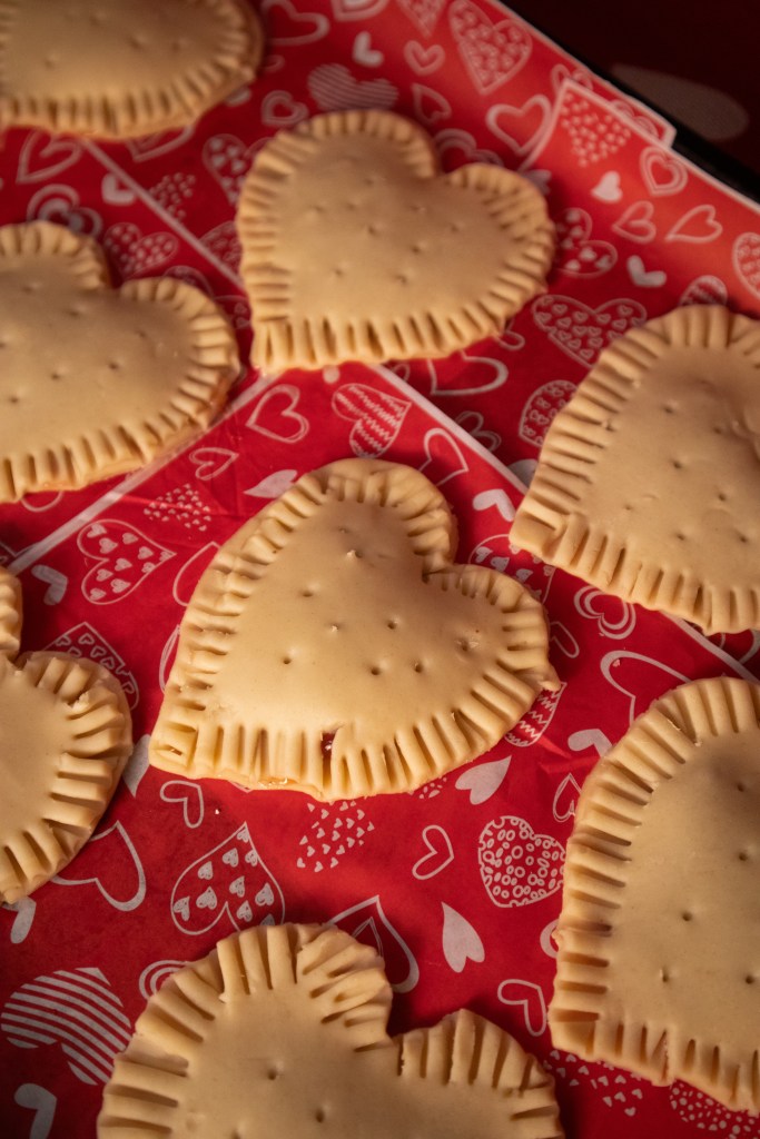 Baked heart-shaped pop tarts displayed on red paper with heart patterns.