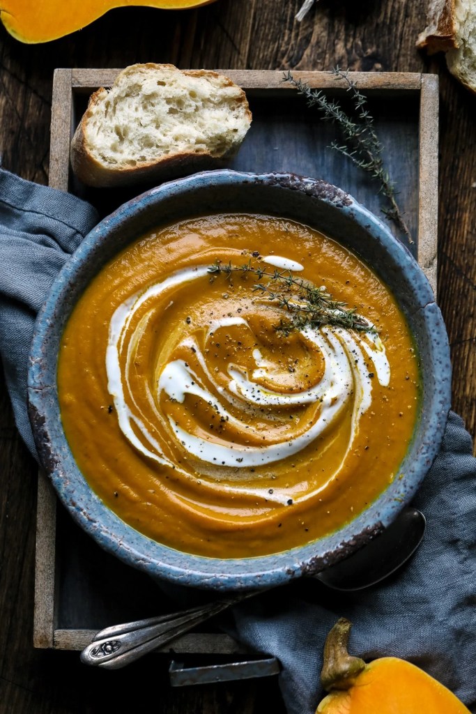 Velvety roasted butternut squash soup garnished with fresh herbs and a swirl of cream served in a rustic bowl
