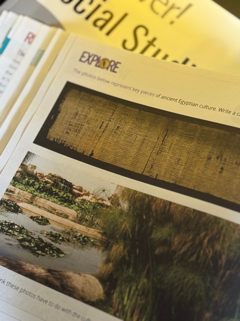 A close-up view of a page from the Discover! Social Studies curriculum featuring two images related to ancient Egyptian culture. The top image displays ancient Egyptian writing on a scroll, while the bottom image shows a serene water landscape with lily pads and greenery.
