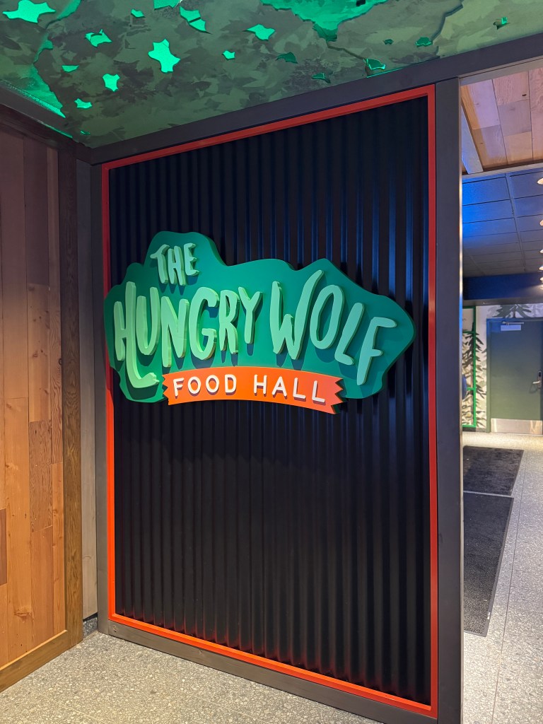 Sign for 'The Hungry Wolf Food Hall' at Great Wolf Lodge, featuring a colorful design with green lettering on a black background.