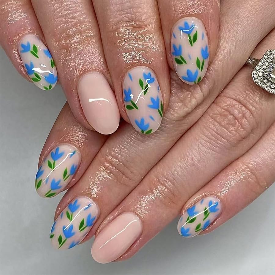 A close-up of manicured hands with a nail design featuring blue flowers and green leaves on a clear background, along with a nude-colored nail.