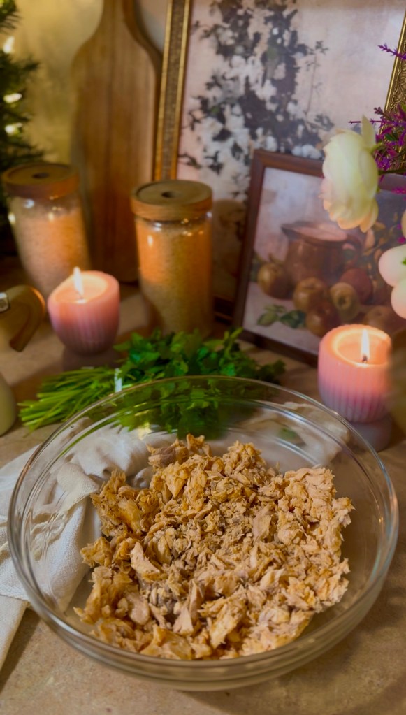 A bowl of shredded salmon placed on a countertop decorated with candles, jars, and framed art, creating a cozy kitchen atmosphere.
