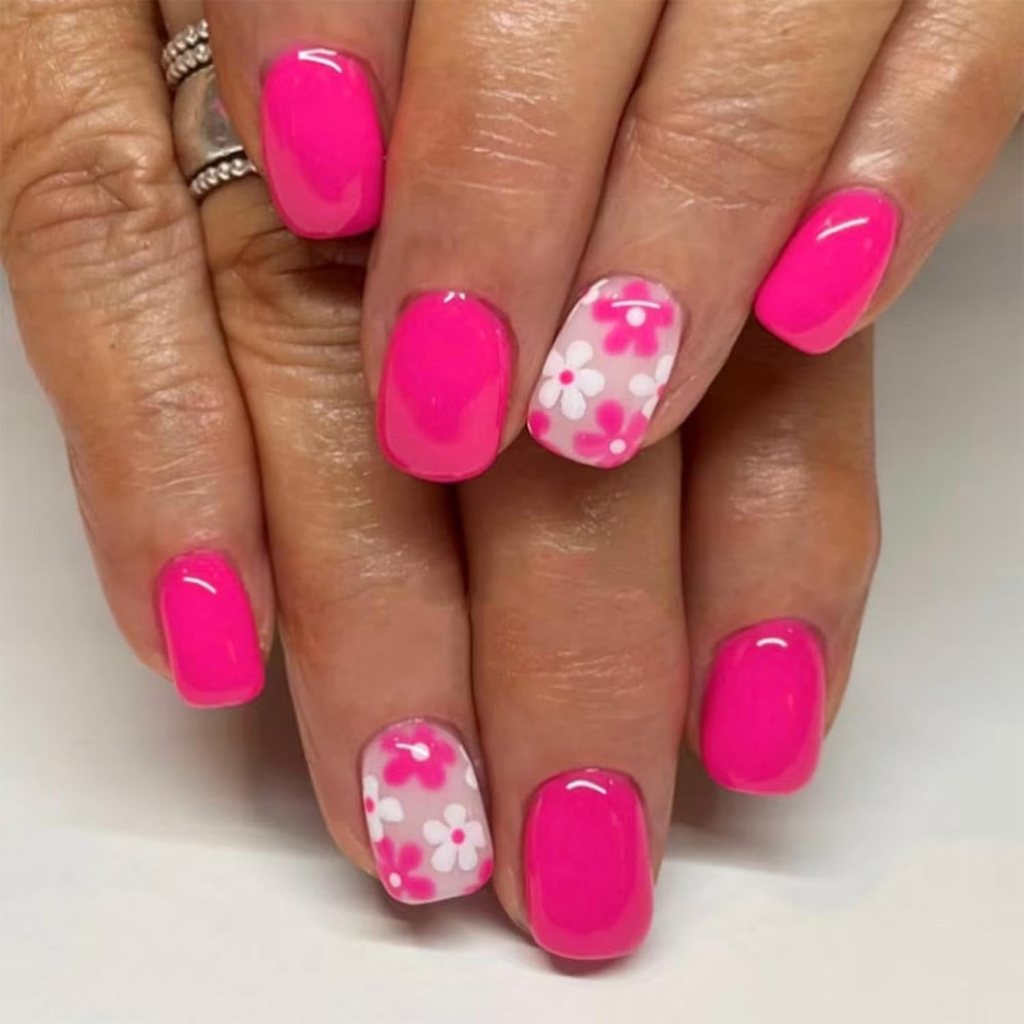 Close-up of hands with bright pink nail polish and one accent nail featuring white and pink floral designs.