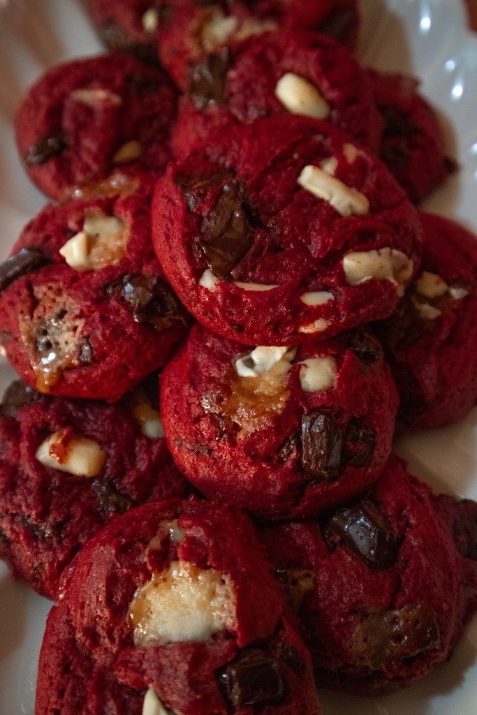 A close-up view of a plate stacked with red velvet cookies, featuring chunks of dark chocolate and white chocolate chips.