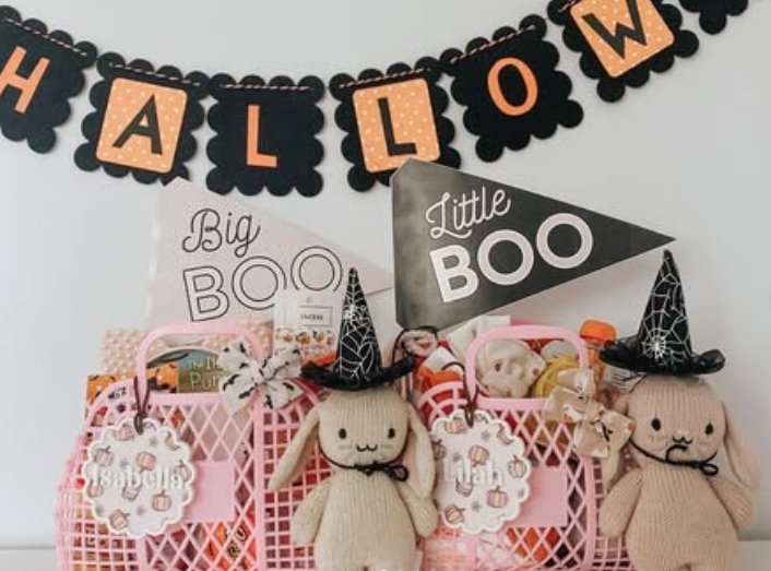 Two pink baskets labeled 'Big Boo' and 'Little Boo' filled with Halloween goodies and plush toys, featuring a 'HALLOW' banner in the background.
