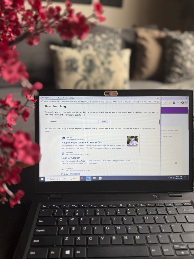 A laptop screen displaying a web browser with search results about puppies, including links to a kennel club and adoption options, with decorative flowers in the foreground.