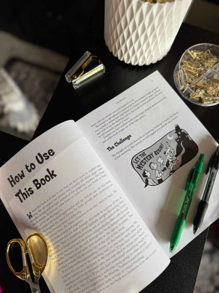 An open book titled 'How to Use This Book' with text and an illustration on the page, accompanied by a pair of scissors, two pens, and a stapler on a dark surface.