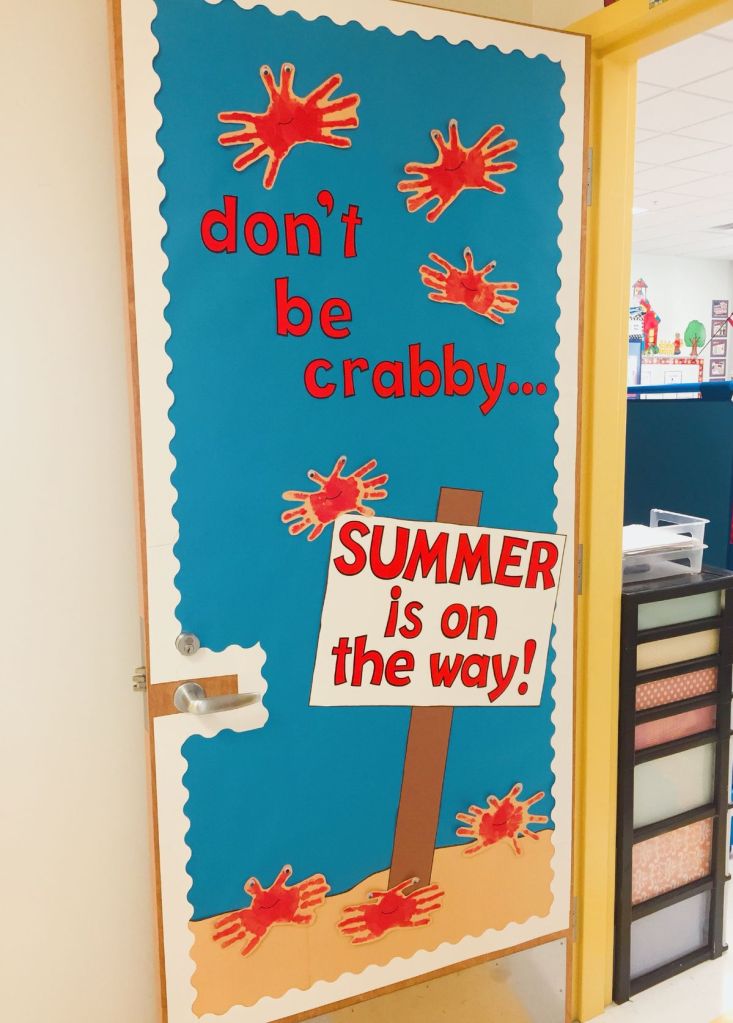 A colorful door decoration featuring a blue background, red handprints, and a sign that reads "don't be crabby... SUMMER is on the way!"