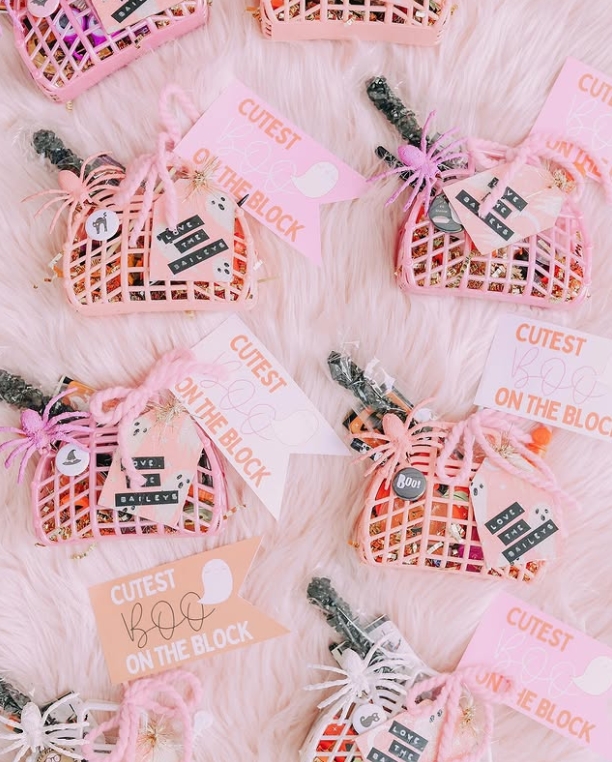 A collection of pink boo baskets arranged on a fluffy surface, each filled with festive treats and decorated with tags that read 'Cutest Boo on the Block' and personalized names.