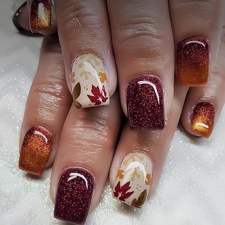 A close-up of manicured hands showcasing fall-inspired nails with a mix of deep burgundy, orange, and glossy glitter finishes, featuring hand-painted autumn leaves in warm colors.