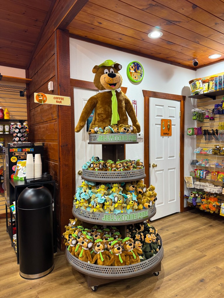 A display of plush toys featuring a large teddy bear and smaller bear characters in a gift shop, with a coffee bar sign visible in the background.